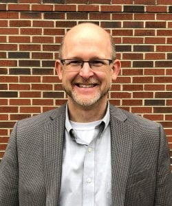 Asenka team member Brian Hasenkamp in front of a brick wall